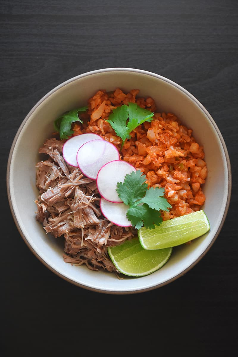 A Whole30 burrito bowl with Mexican Cauliflower Rice, carnitas, sliced limes, and radishes offers a healthy take on a popular dish.