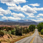 A view down the highway on the High Road, partly cloudy skies and green trees covering the high desert