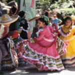 Children in traditional Mexican clothing dancing at a Cinco de Mayo celebration.