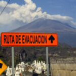 Close-up of a warning sign with an illustration of a person running away from an erupting volcano, symbolizing evacuation routes around Popocatepetl