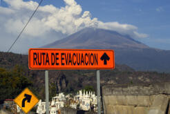 Close-up of a warning sign with an illustration of a person running away from an erupting volcano, symbolizing evacuation routes around Popocatepetl