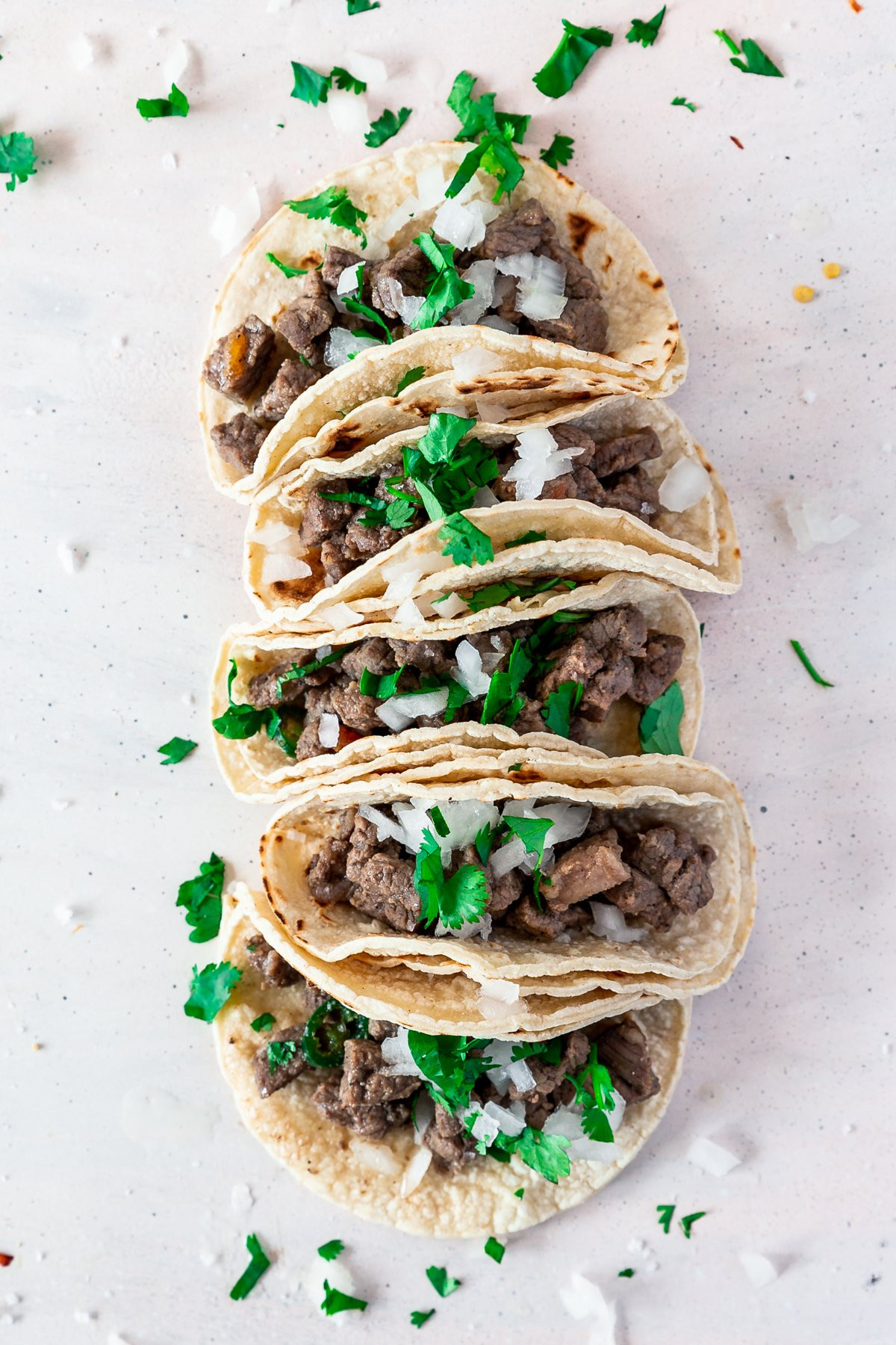 overhead view of carne asada mexican street tacos, in a double layer of crispy corn torillas and sprinkled with cilantro and onion.