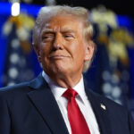 Donald Trump smiles in a navy suit and red tie