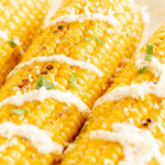 Elote (Mexican corn on the cob) drizzled with crema on a white plate.