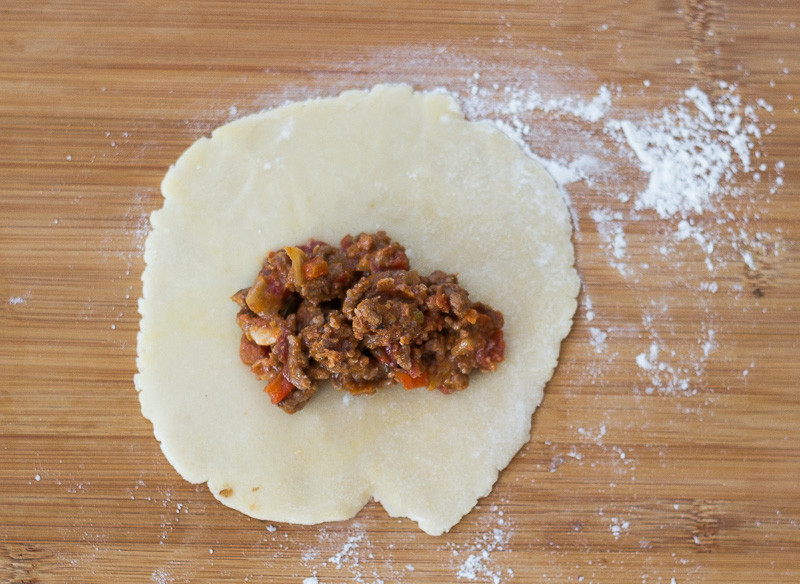 Preparing Mexican empanadas by adding meat filling to rolled-out dough circles