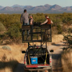 hunters stand in platform above pickup truck