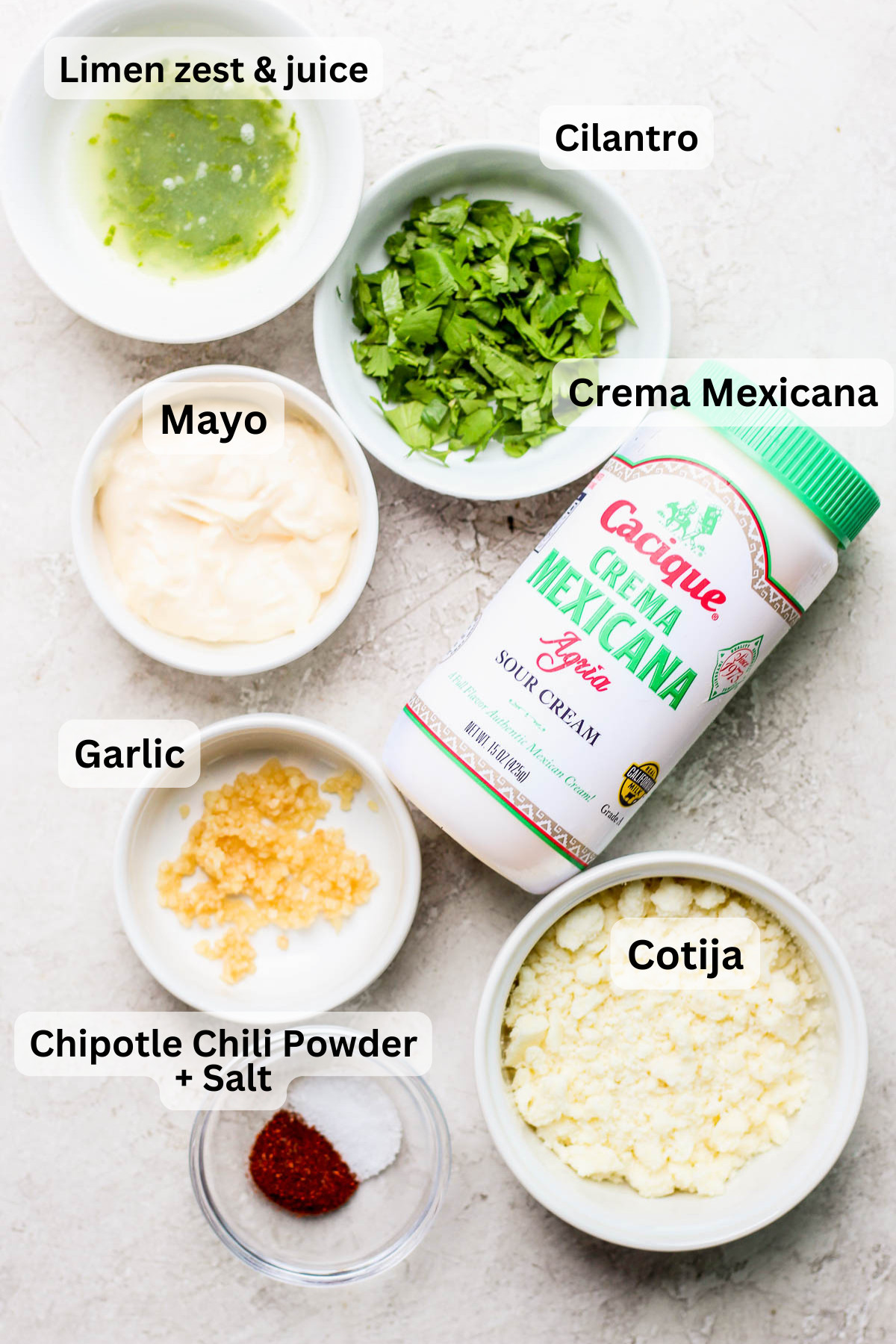 Ingredients needed to make elote, including corn, mayonnaise, crema, cotija cheese, lime, cilantro, and chili powder