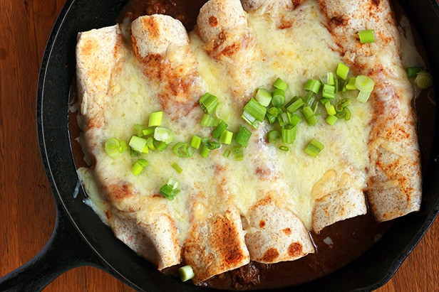 Enchiladas in a cast iron pan topped with cheese and sauce