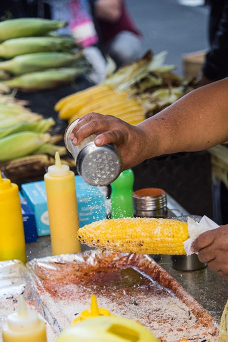 Hands preparing Elote with various toppings