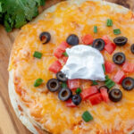 Overhead shot of two Mexican pizzas sitting on a wooden surface, garnished with fresh diced tomatoes and green onions.