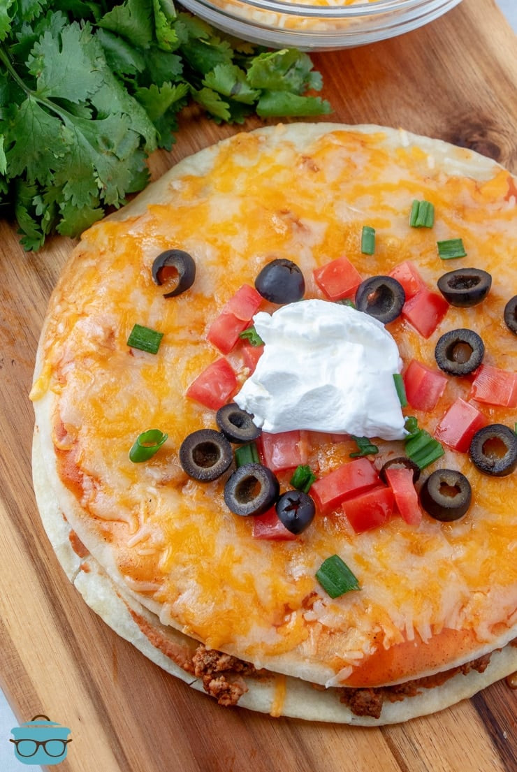 Overhead shot of two Mexican pizzas sitting on a wooden surface, garnished with fresh diced tomatoes and green onions.