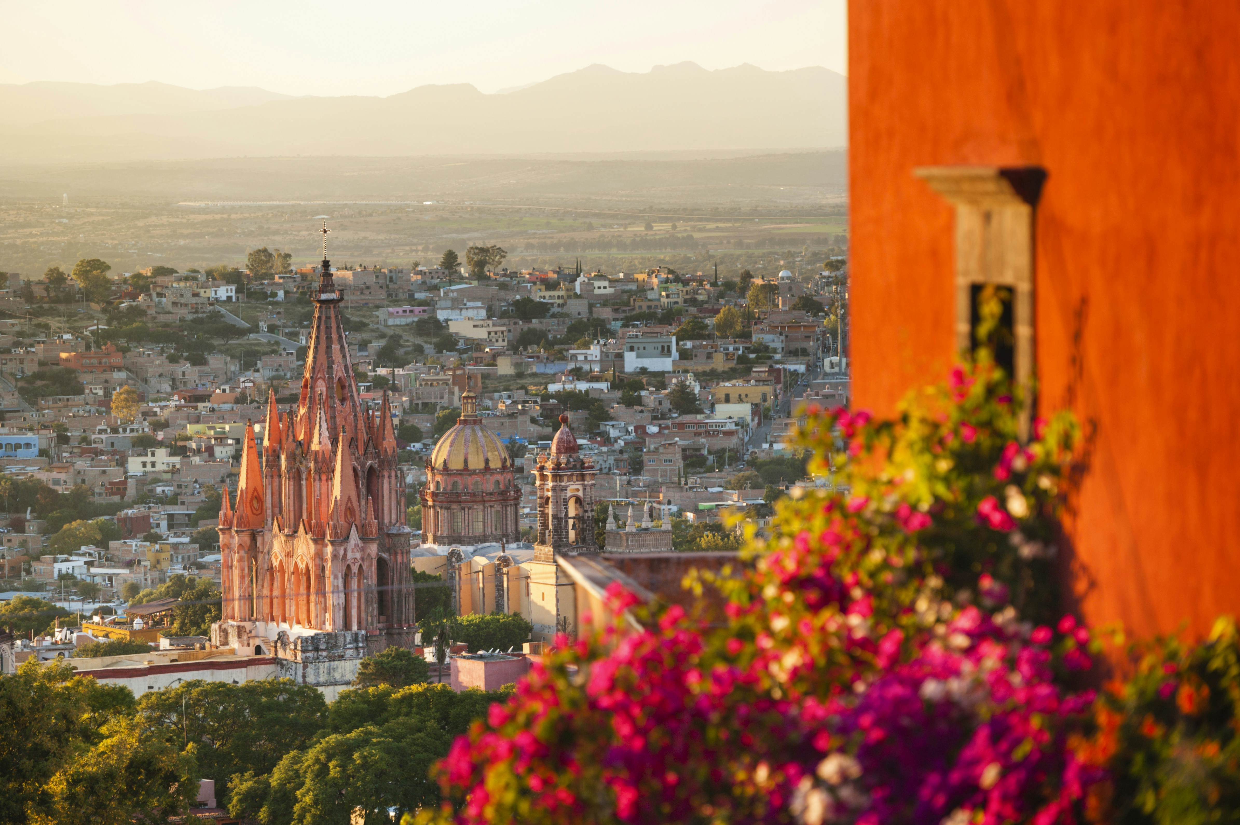A church is seen below from a terrace, with bougainvillea and an orange wall that is illuminated by the setting sun.