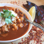 Menudo in a bowl with traditional garnishes like cilantro, onions, and lime