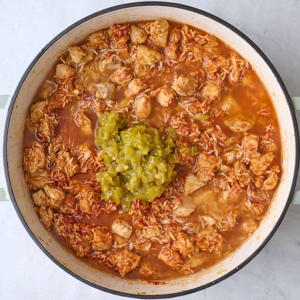 Adding green chilies and water to Mexican rice and chicken