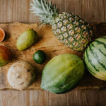 A variety of colorful fruit arranged on a wooden board, including mango, jicama, papaya, pineapple, and watermelon.