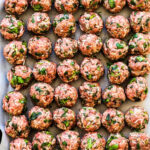 Rows of perfectly formed, uncooked albondigas meatballs, seasoned with fresh herbs and spices, ready to be added to a simmering pot of authentic Mexican meatball soup.