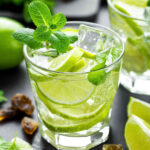 A glass of Mexican mojito with lime slices floating in it and a mint sprig garnish.