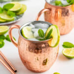 Two copper mugs filled with a Mexican Mule cocktail, showcasing the drink's bubbly texture and lime wedge garnish