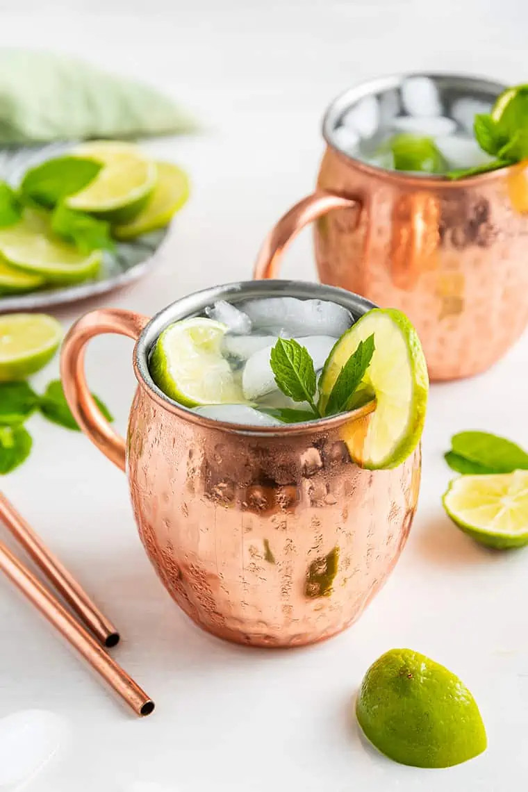 Two copper mugs filled with a Mexican Mule cocktail, showcasing the drink's bubbly texture and lime wedge garnish