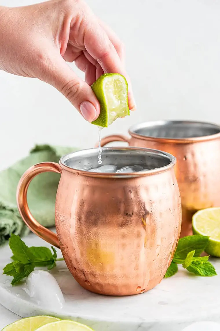 A hand squeezing fresh lime juice into a copper mug containing a Mexican Mule cocktail, showcasing the final step in preparation