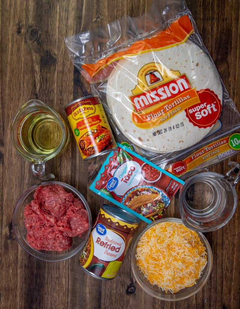 Ingredients for making Mexican pizza, including ground beef, taco seasoning, refried beans, enchilada sauce, cheese, and flour tortillas.