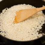 Long grain white rice toasting in a pan, a wooden spoon for mexican rice