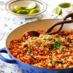 Authentic Mexican rice served with lime wedges in a blue skillet, showcasing its vibrant color and texture.