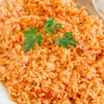 Authentic Mexican Rice recipe on a platter with a wooden spoon, a sprig of parsley, showcasing the vibrant colors and textures