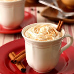 Mexican Mocha in a white mug on a red plate. The warm beverage is garnished with whipped cream and a sprinkle of cinnamon, ready to be enjoyed.
