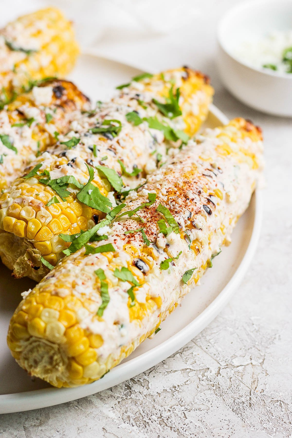 Mexican street corn on the cob, covered in sauce, cheese, and cilantro