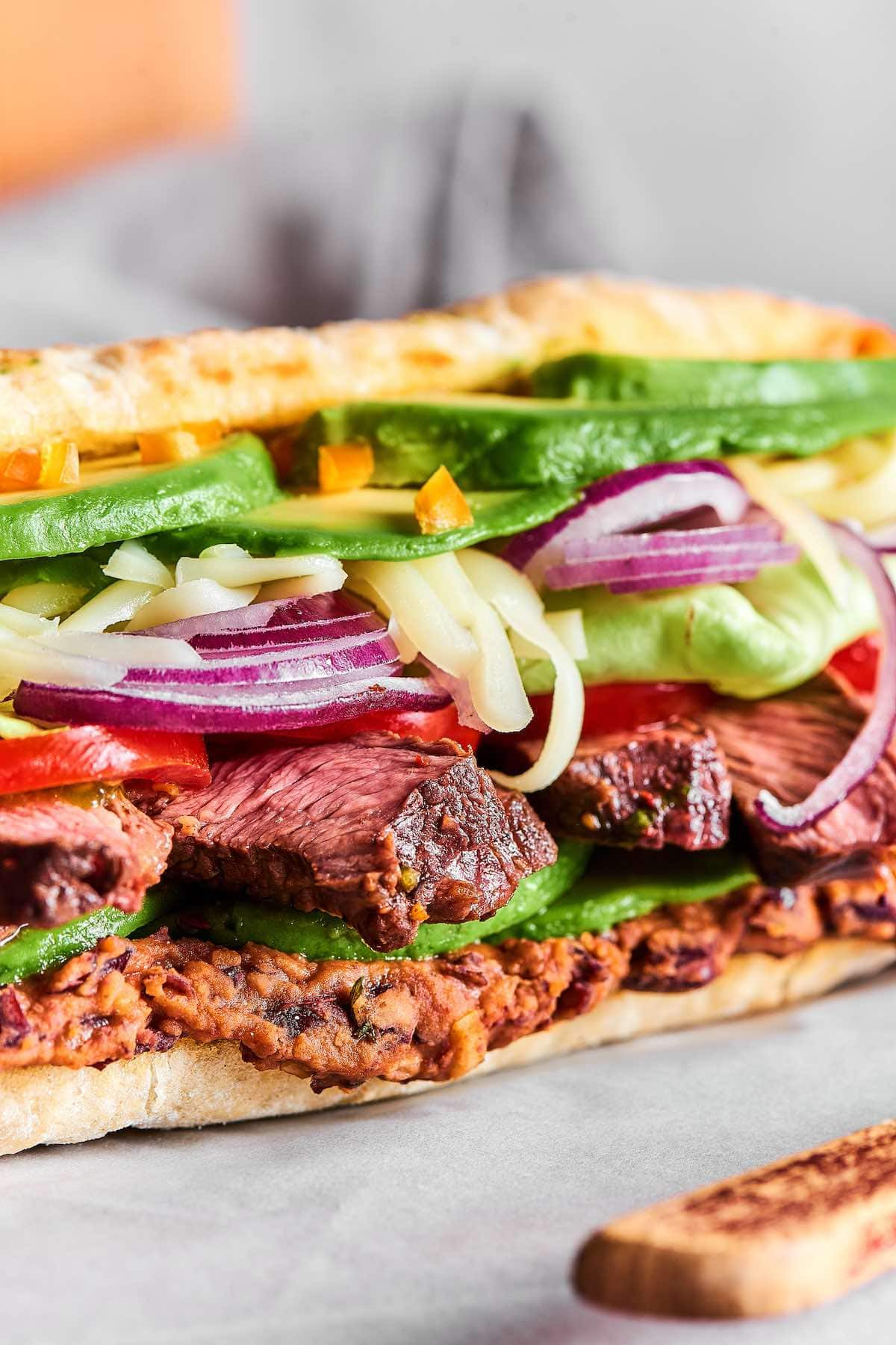 An assortment of colorful Mexican tortas, each featuring different fillings and toppings, displayed on a rustic wooden table.