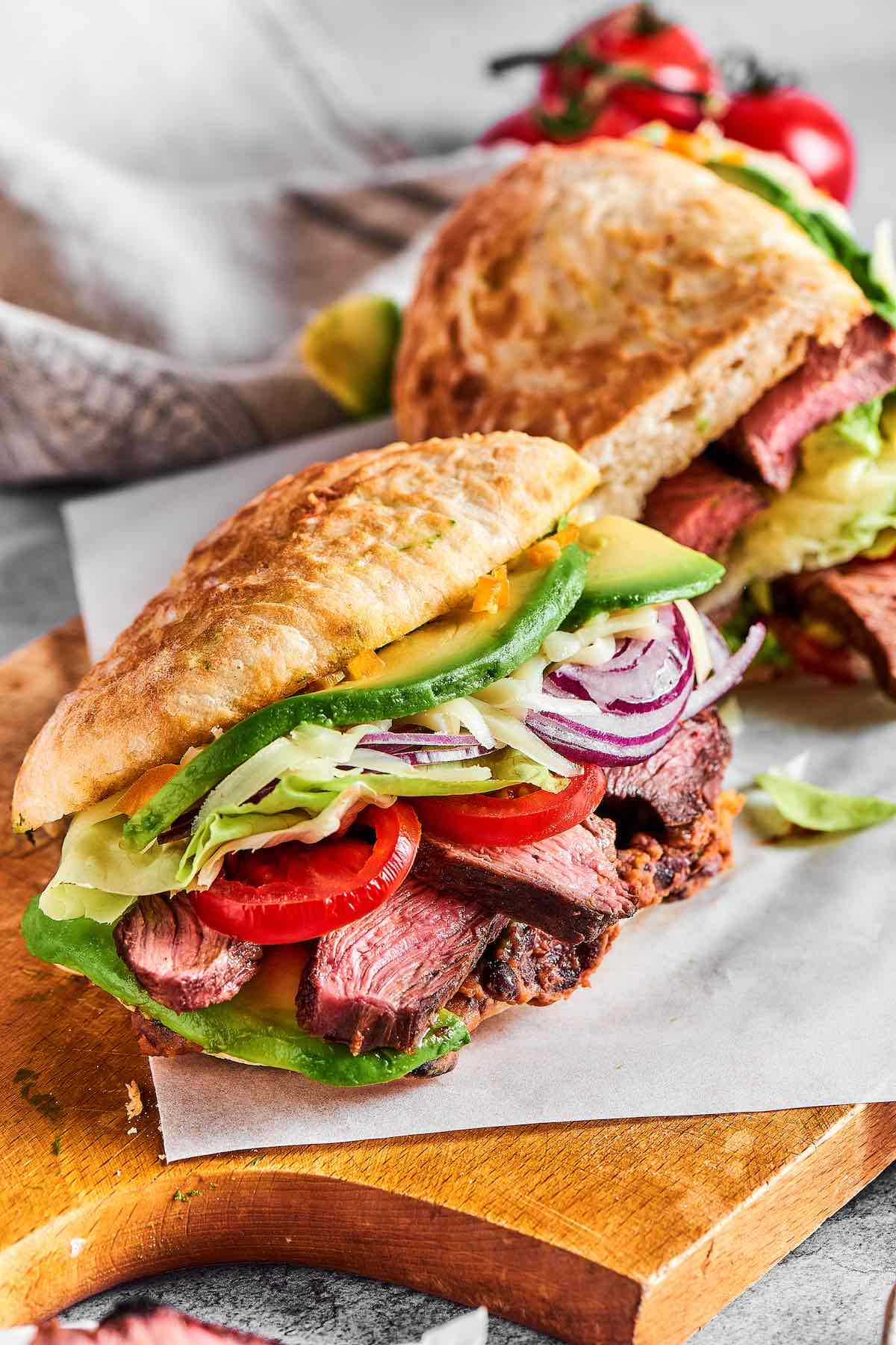 A close-up shot of a perfectly assembled Mexican torta with layers of meat, beans, cheese, and fresh vegetables visible between the crusty bread.