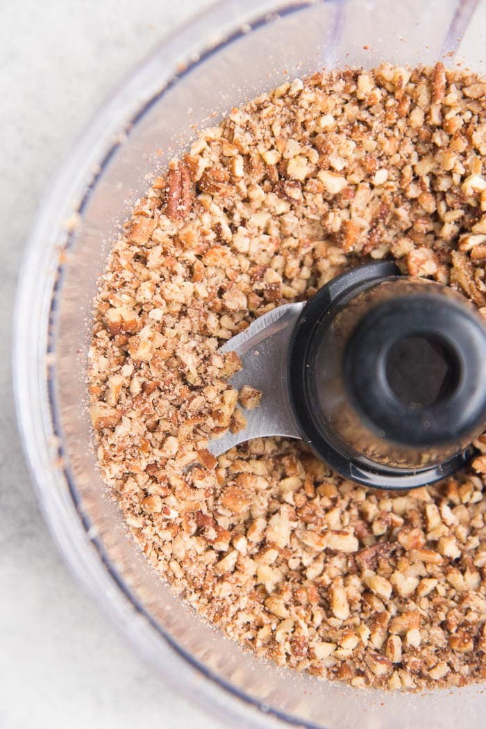 Pecan nuts getting chopped inside a food processor, with finely and coarsely ground nuts visible.