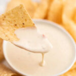 Tortilla chip dipped in a bowl of white queso dip