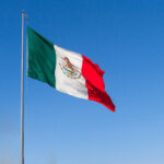 Mexican flag waving proudly against a clear blue sky, showcasing its vibrant green, white, and red colors.