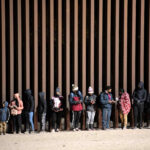 In this Dec. 26, 2022, file photo, asylum-seekers line up to be processed by US Customs and Border Patrol agents at a gap in the US-Mexico border fence near Somerton, Ariz.