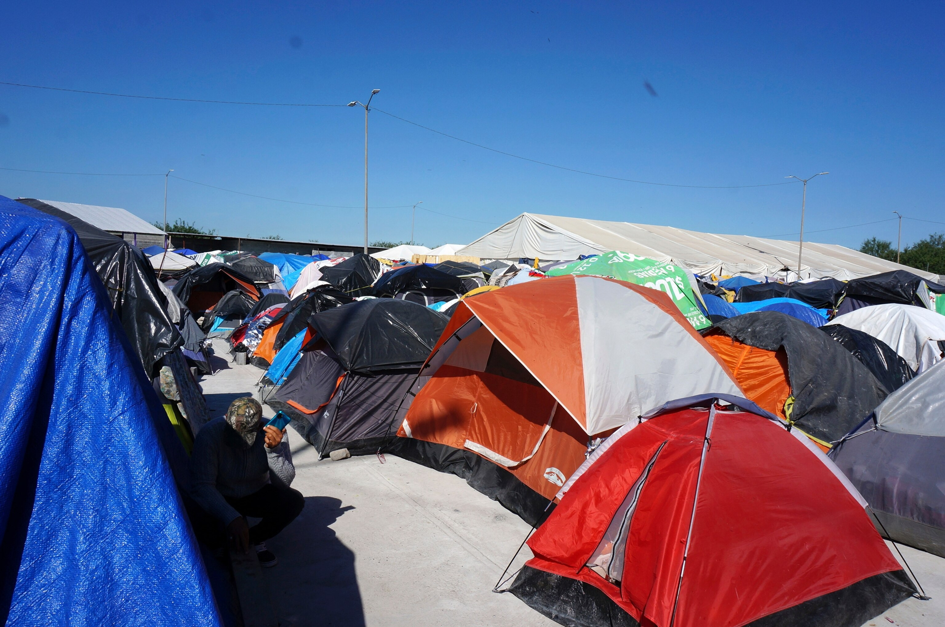 PHOTO: In this Dec. 15, 2022, file photo, a migrant listens to his phone by his tent in the vast, open-air shelter Senda de Vida 2 in Reynosa, Mexico.