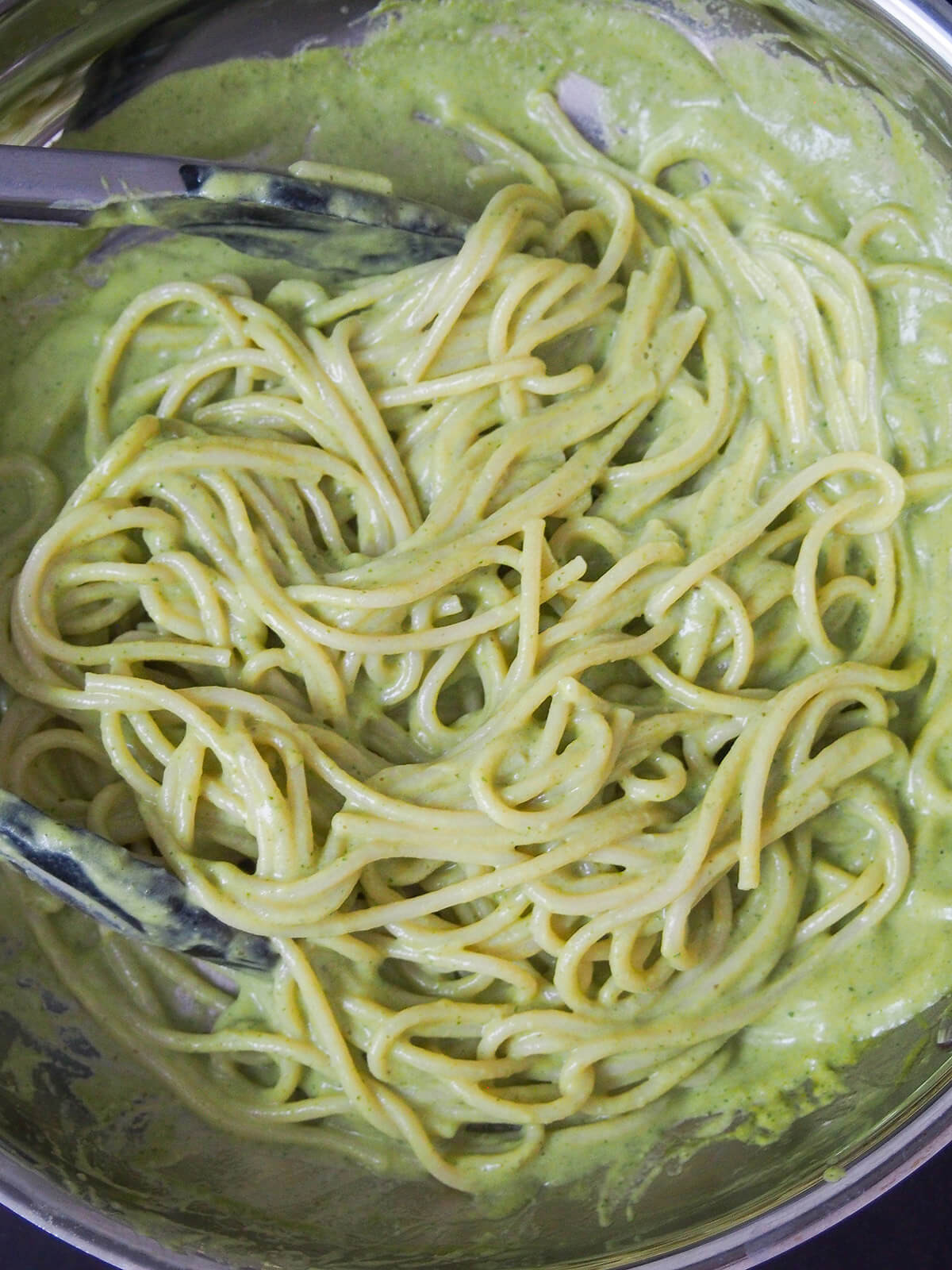 Mixing cooked pasta into the creamy green sauce, showcasing the final steps in preparing Espagueti Verde.