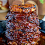 A vibrant street food scene showcasing a vertical spit of al pastor meat, with a chef expertly slicing off thin pieces into awaiting tortillas, surrounded by the bustling energy of a Mexican market. The image captures the essence of authentic Mexican cuisine.