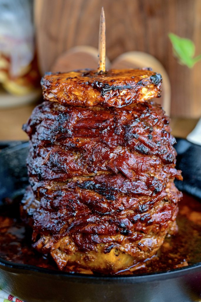 A vibrant street food scene showcasing a vertical spit of al pastor meat, with a chef expertly slicing off thin pieces into awaiting tortillas, surrounded by the bustling energy of a Mexican market. The image captures the essence of authentic Mexican cuisine.