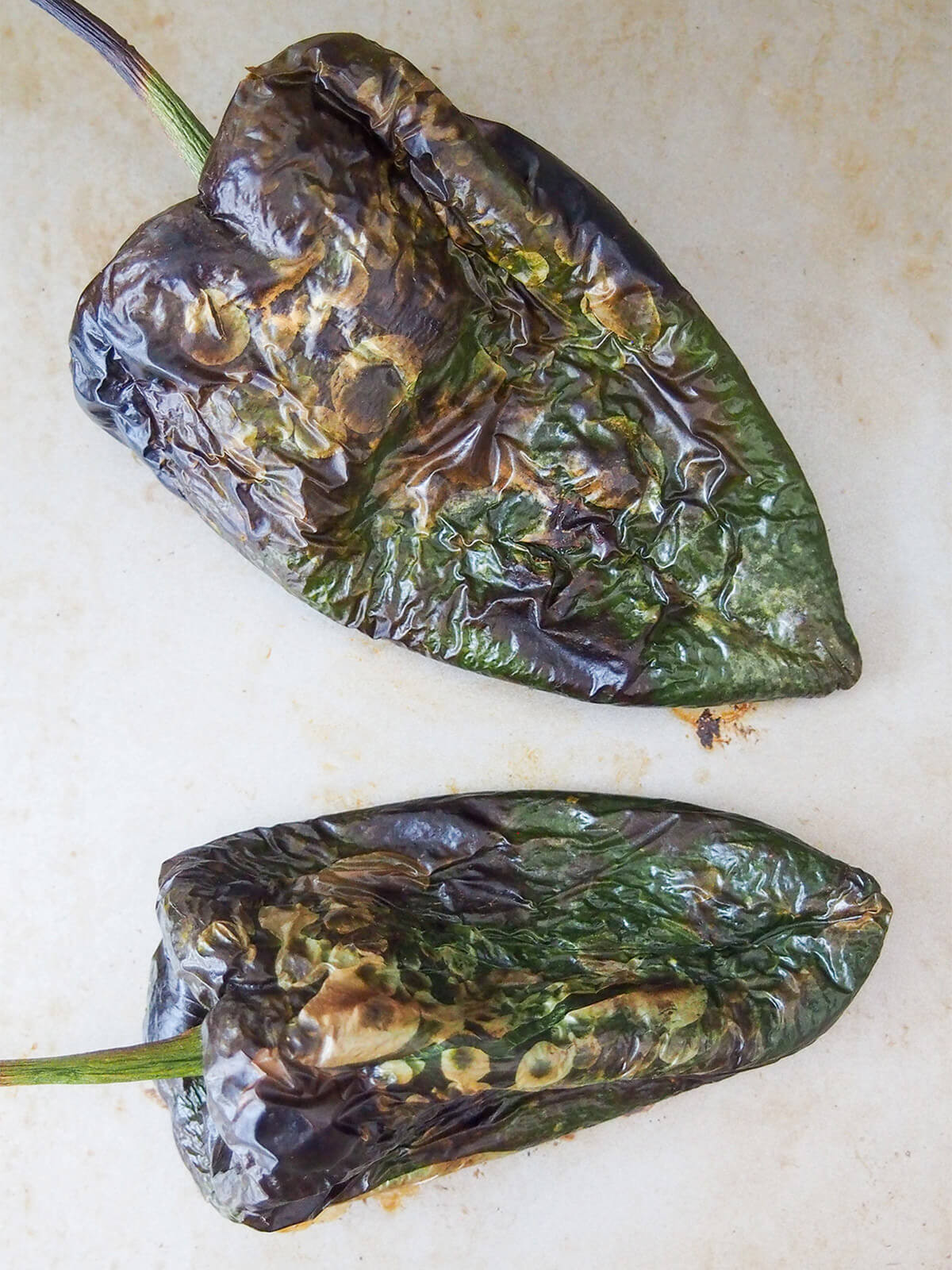 Two roasted poblano peppers on a baking sheet, showing the blackened skin after roasting, which is essential for easy peeling and enhancing the flavor of Espagueti Verde.