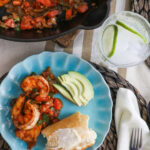 Overhead shot of cooked Camarones a la Mexicana, served over quinoa with avocado slices and a side of lime wedges, garnished with fresh cilantro