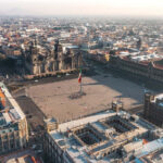 An aerial shot of Plaza de la Constitucion in Mexico with a large Mexican flag in the center.