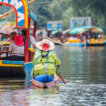 Xochimilco canal with people sailing down it on colorful boats.