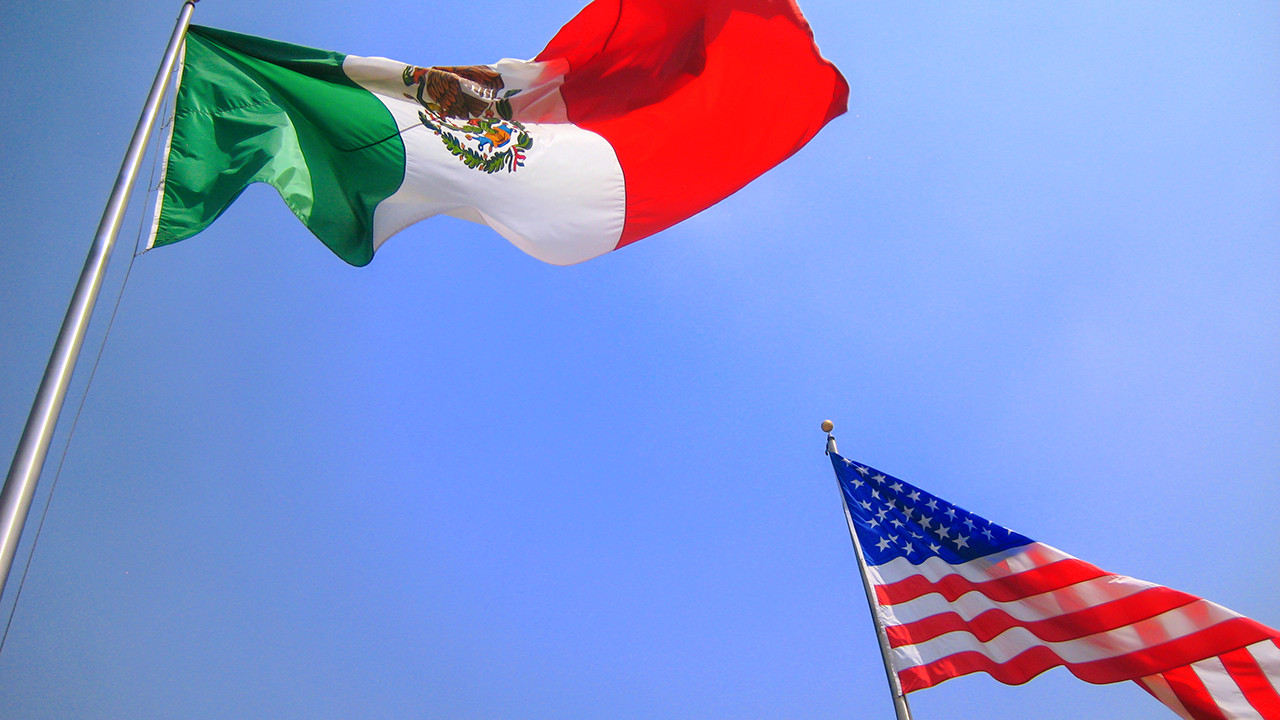 A Mexican and American flag on flagpoles, representing the complex relationship between the two countries.