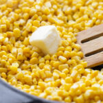 Corn kernels piled in a cast iron skillet with butter on top.
