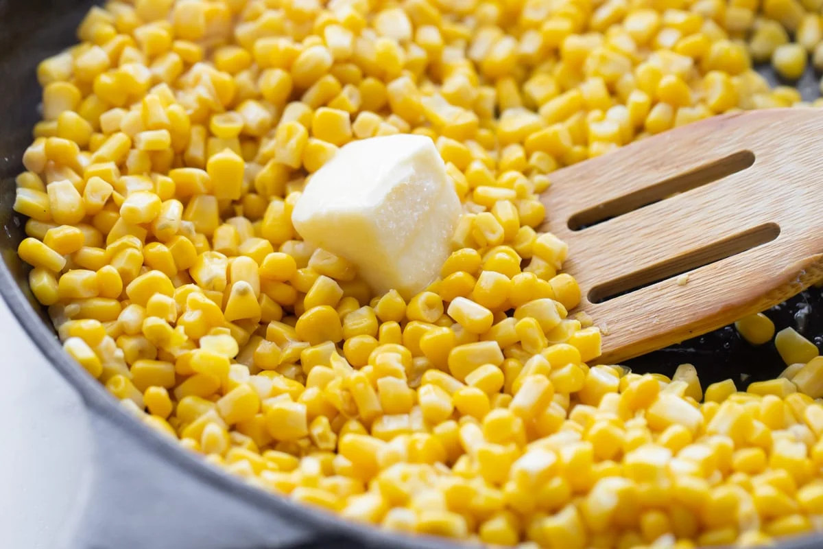 Corn kernels piled in a cast iron skillet with butter on top.