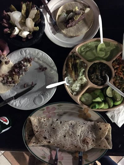 A table spread featuring a variety of Mexican dishes, including tortillas filled with grilled meat, a rolled burrito, and a platter with different salsas, guacamole, cucumbers, and roasted vegetables, Super Burro showcasing a giant tortilla with perfectly grilled arrachera (steak) and cheese.