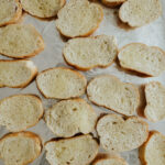 Buttered bread slices on a foil-lined baking sheet for making capirotada.