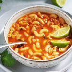 A white bowl of soup with a lime on the side.